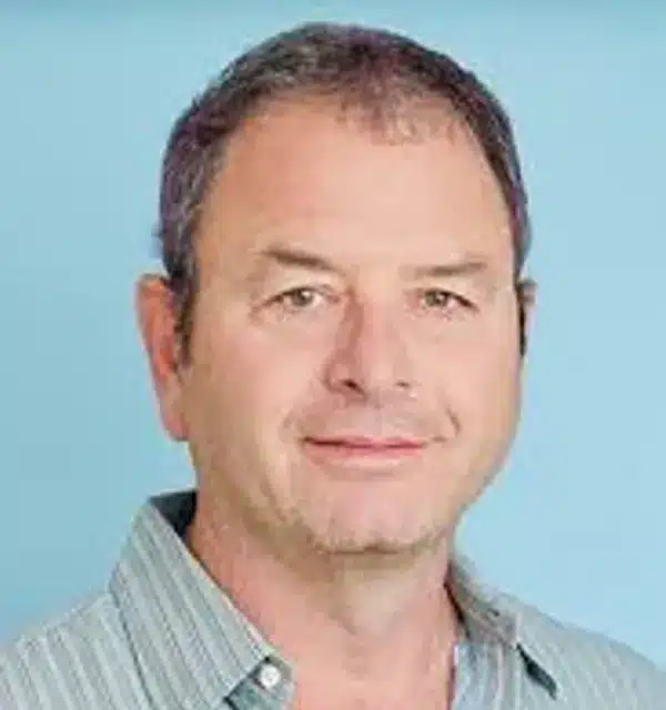 man with short hair and a striped shirt smiles against a light blue background.