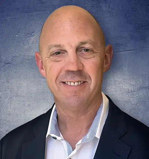smiling bald man in a suit poses against a textured blue background.